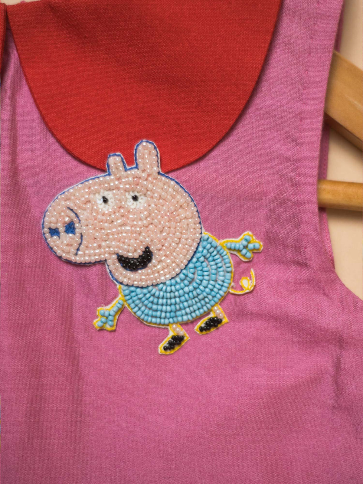 Close-up of Peppa’s Pocket Dress highlighting the hand-embroidered Peppa Pig character motif peeking out from a vibrant red patch pocket.
