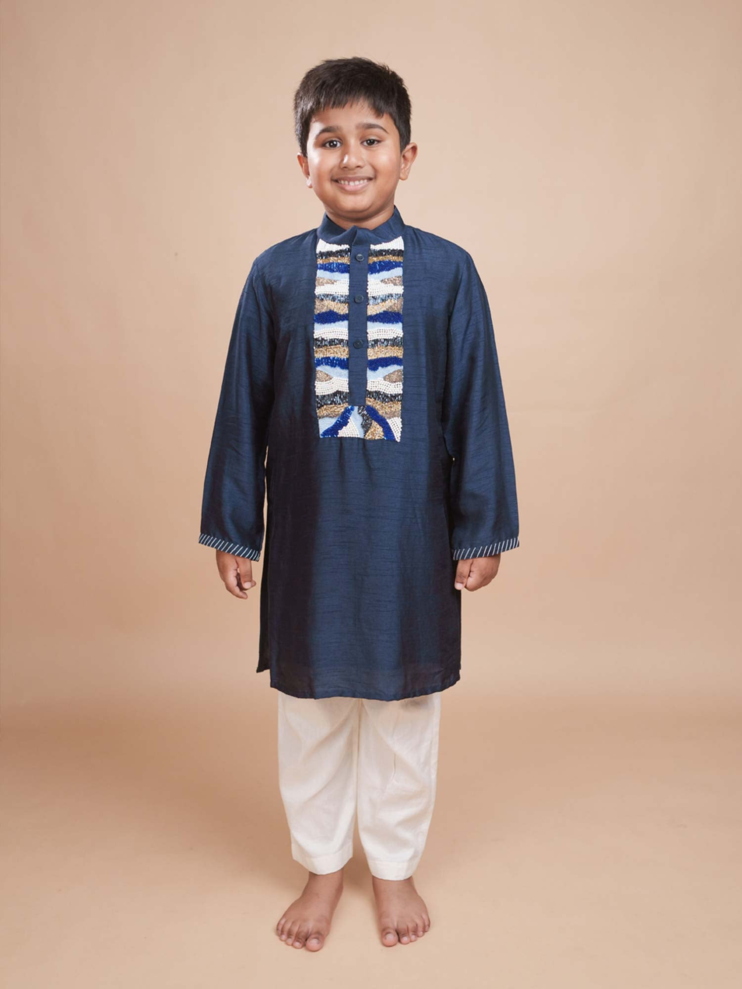Young boy modeling the Neel Kurta Magic navy blue bamber silk kurta with gold, blue, and white embroidery and white pants.