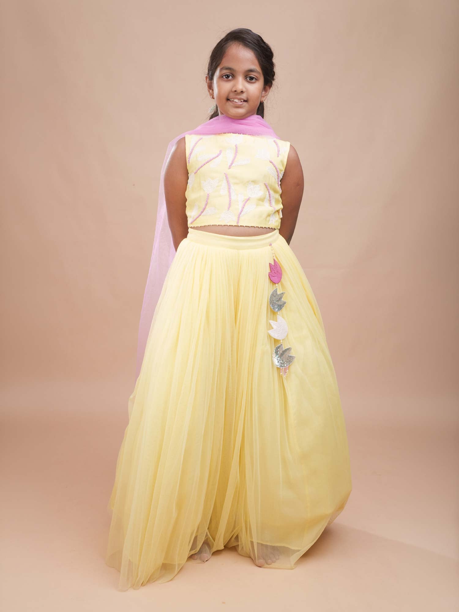 Young girl modeling the Pastel Yellow Tulip Lehenga Set featuring a sleeveless embroidered blouse and a flared net skirt.
