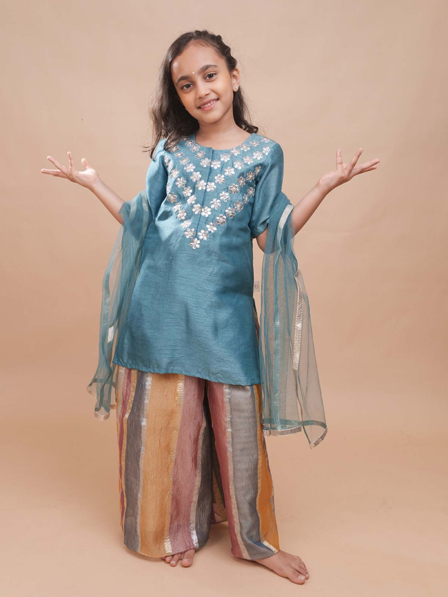 Young girl modeling the Meher teal bamber silk kurta with silver gota patti embroidery and pastel multicolor striped sharara pants.