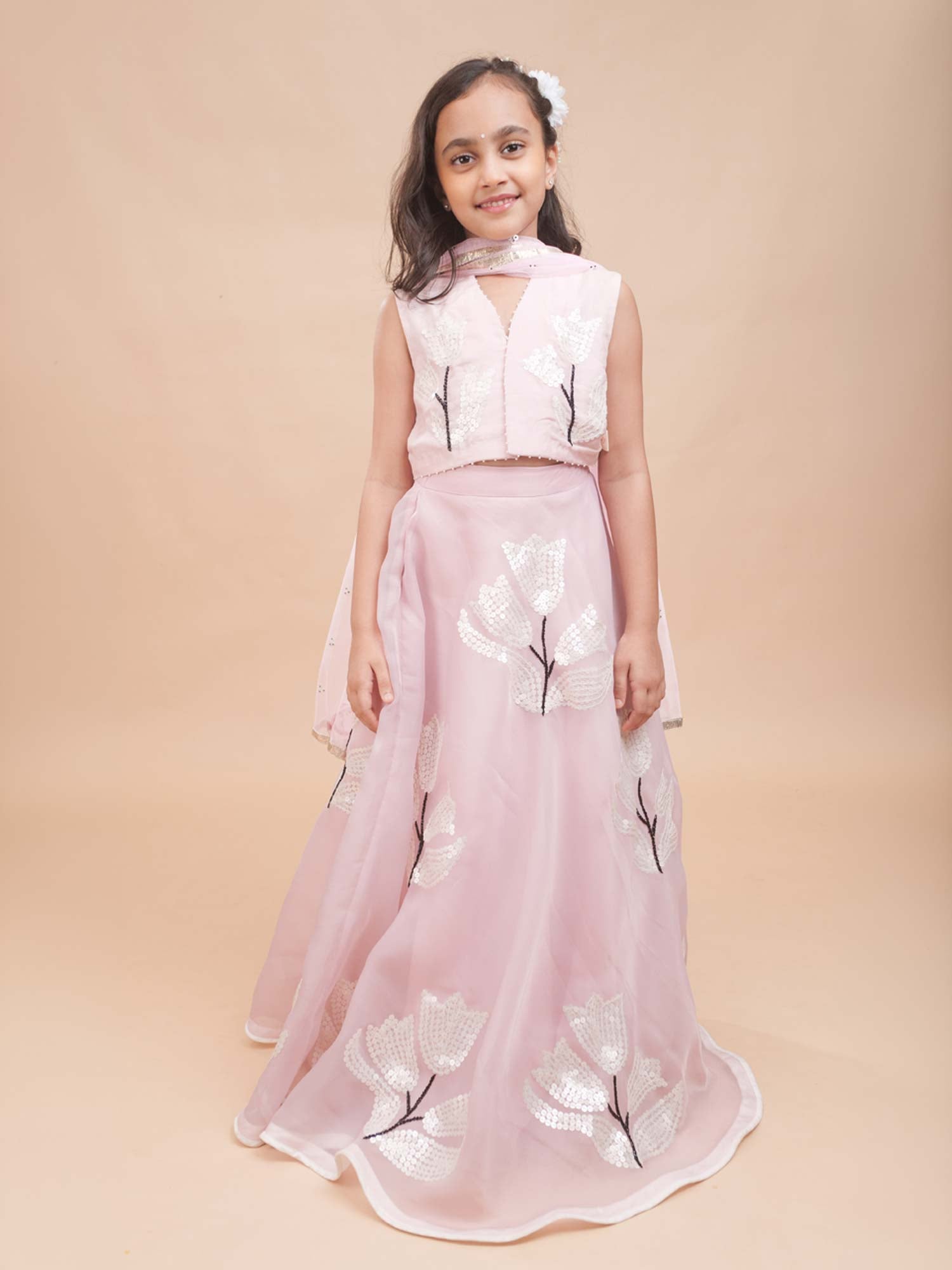 Young girl modeling the Blush Tulip Lehenga Set featuring a sleeveless pink blouse and a flared organza skirt.  