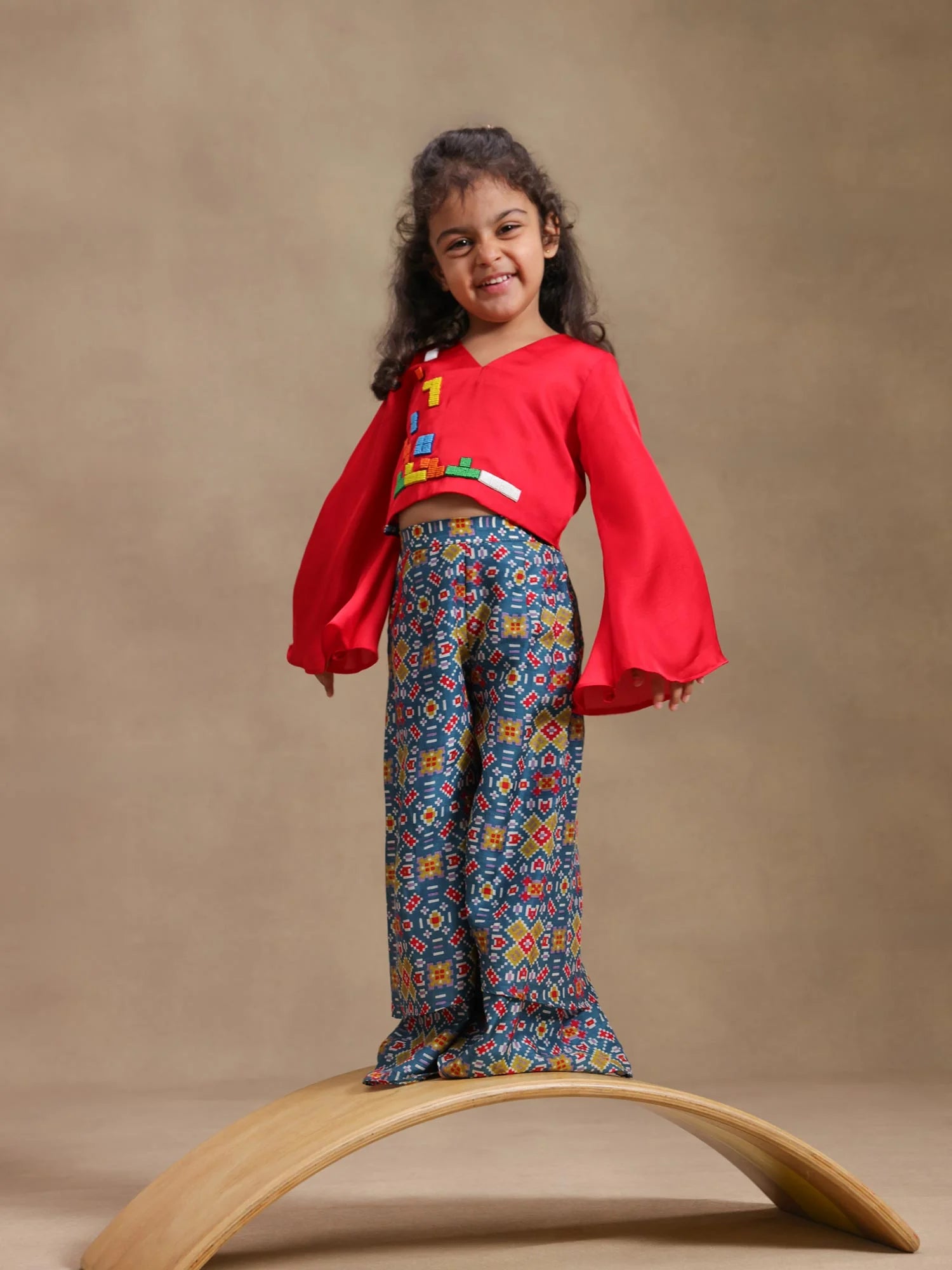 Girl wearing Storytellers Junior Tetris Tales Co-ord Set in red with geometric embellishments and palazzo pants