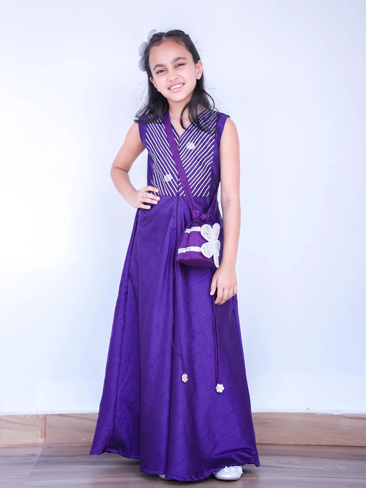 Girl wearing Storytellers Junior Sitara Purple Festive Jumpsuit with gota detailing and potli bag