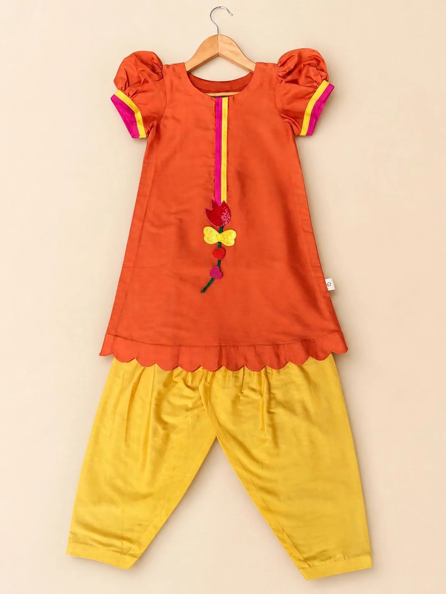 Girl wearing Storytellers Junior Megh Orange Kurta Set with yellow salwar and puff sleeves
